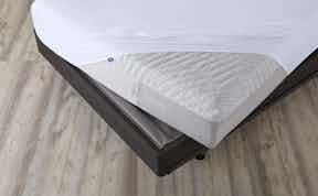 Corner of Wave Hybrid mattress covered by a mattress protector on a foundation and metal bed frame