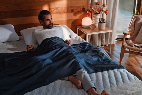 Man lounges comfortably on a Wave Hybrid Snow mattress bed while covered with a Hyperlite sheet. 